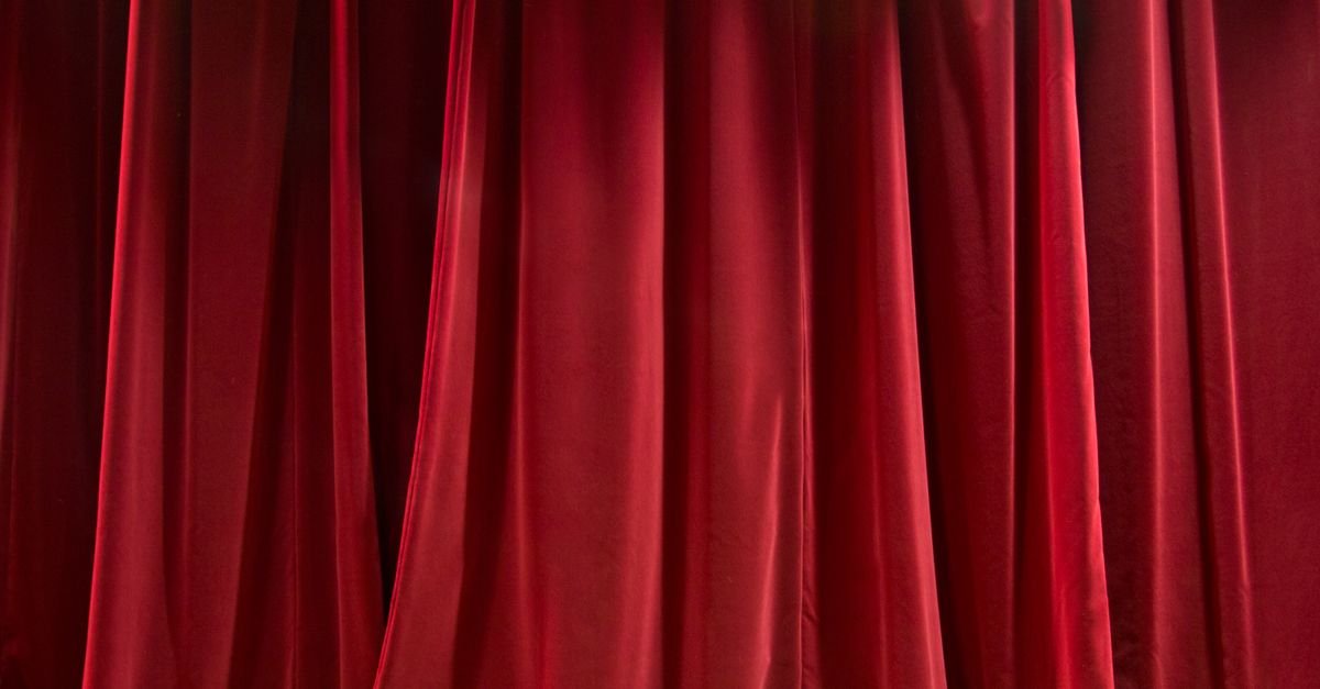 Cortina de teatro de veludo vermelho fechada, iluminada de frente