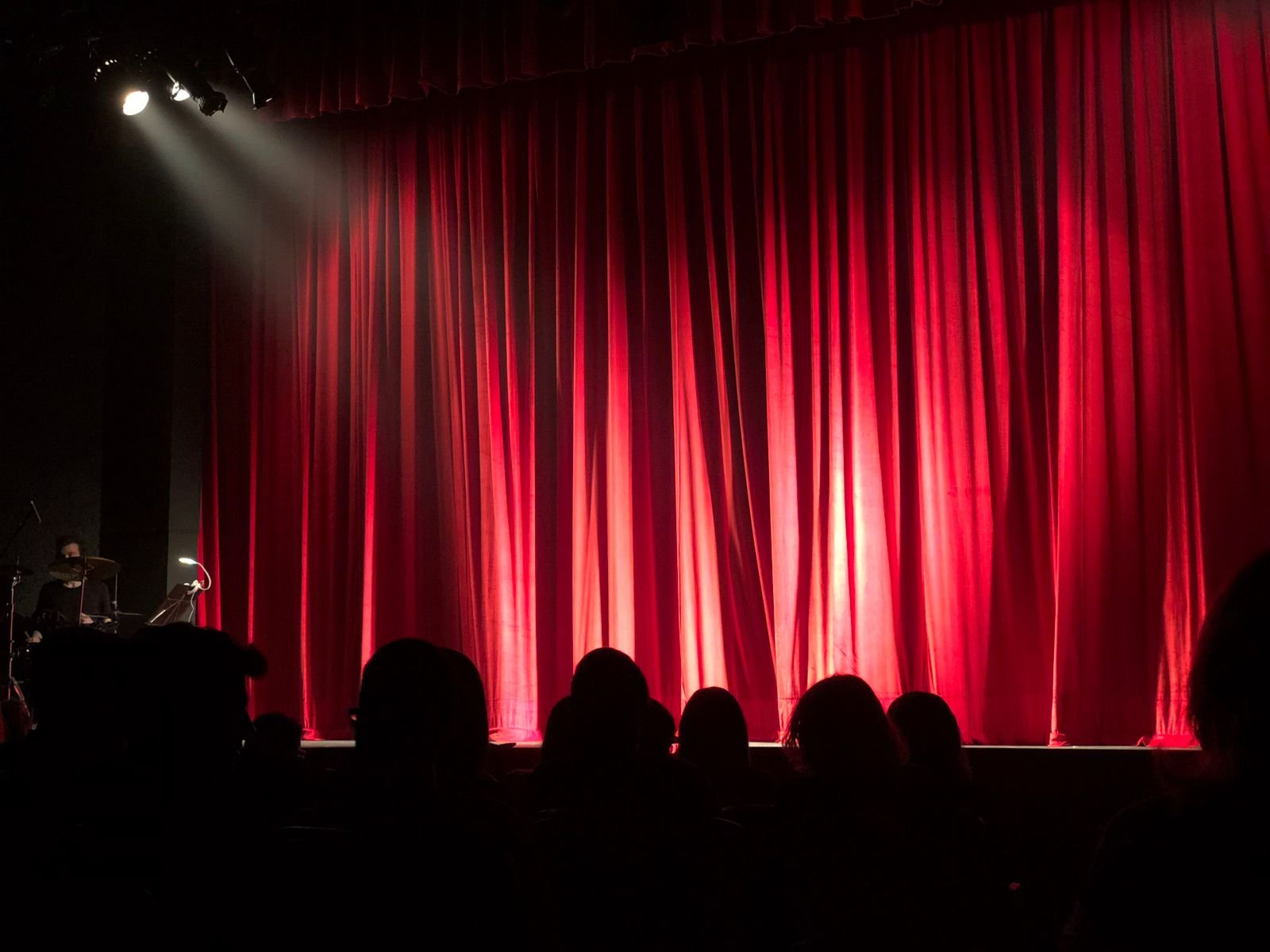 Palco de teatro com cortina vermelha iluminada e plateia em silhueta