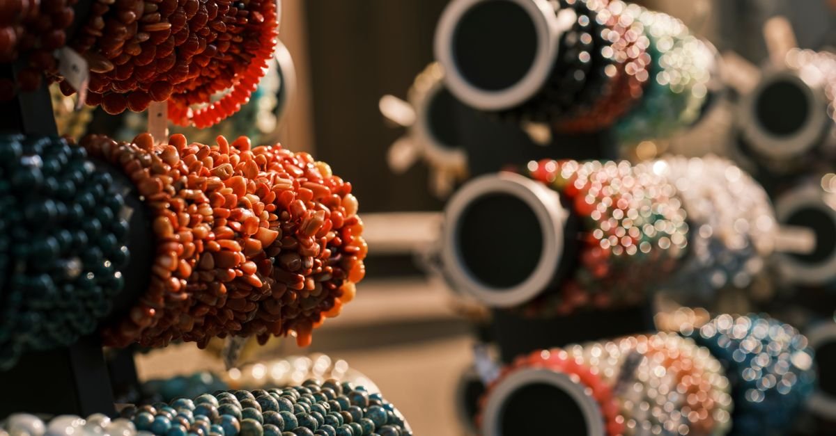 Pulseiras artesanais de pedras coloridas expostas em suportes de banca de feira