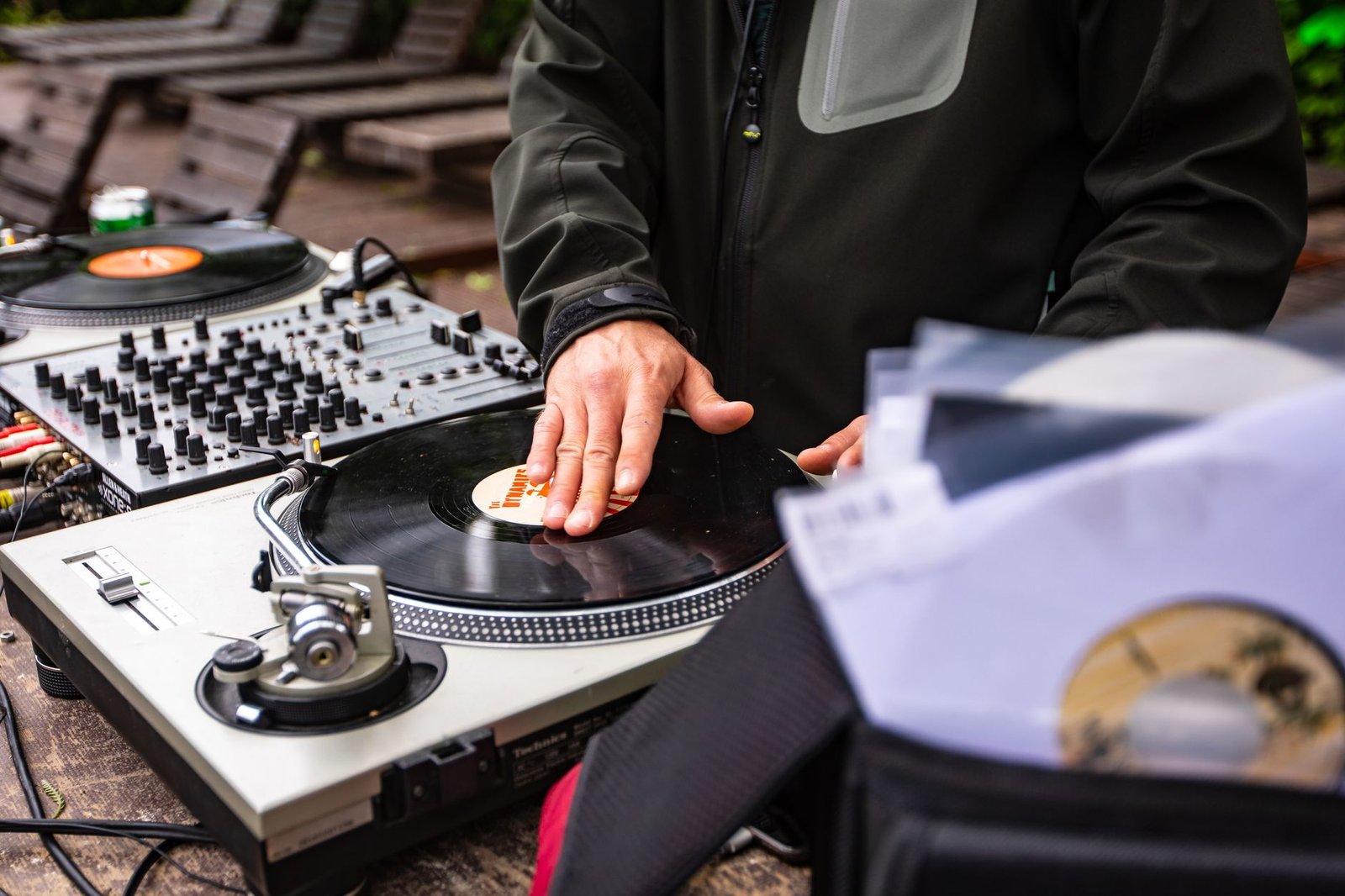 Mãos de um DJ sobre um disco de vinil em toca-discos, com caixa de discos em primeiro plano