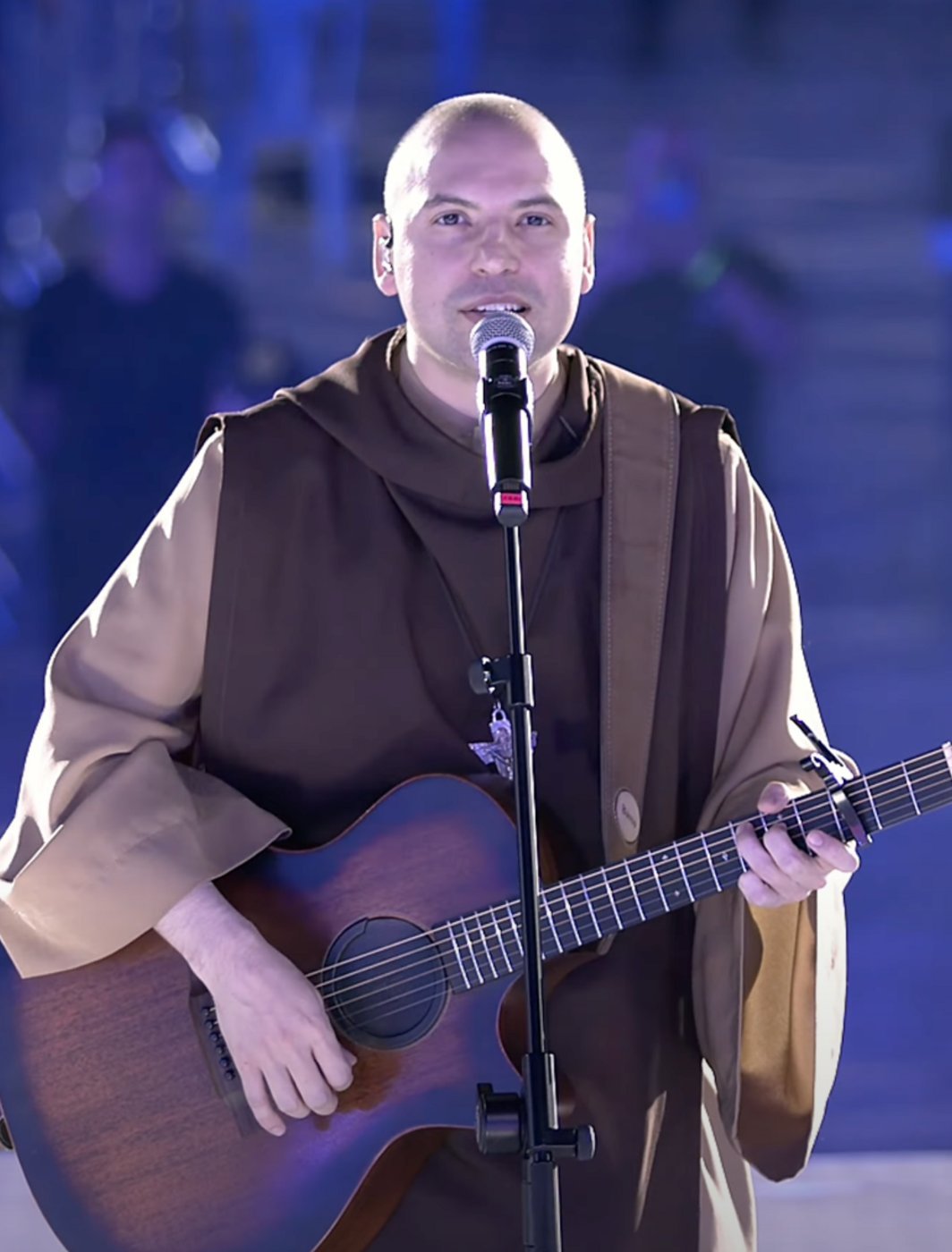 Frei Gilson, de hábito marrom, canta ao microfone com um violão durante apresentação do Desperta Brasil