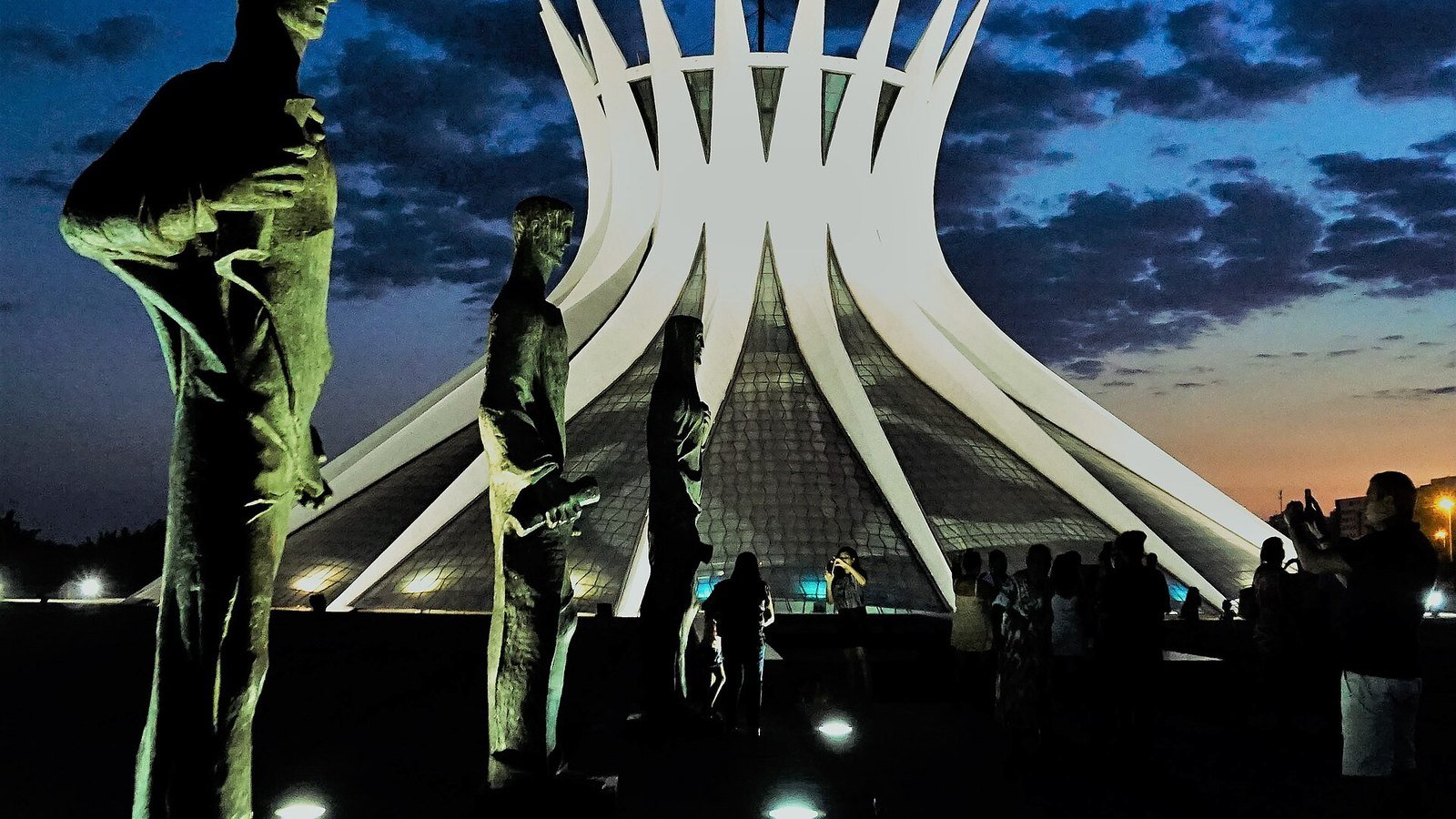 Catedral Metropolitana de Brasília ao entardecer, com as esculturas dos quatro evangelistas à frente; foto de 2017