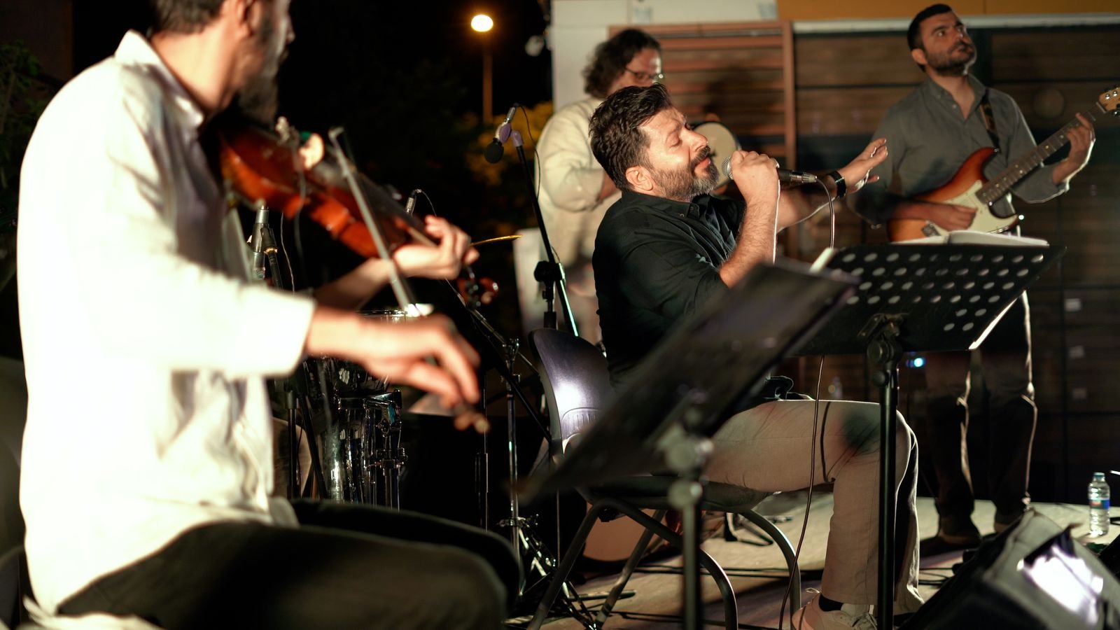 Banda tocando ao vivo à noite, com violino, voz e guitarra
