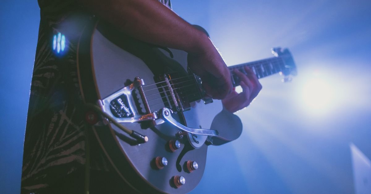 Guitarrista tocando guitarra elétrica em close sob luzes azuis de palco