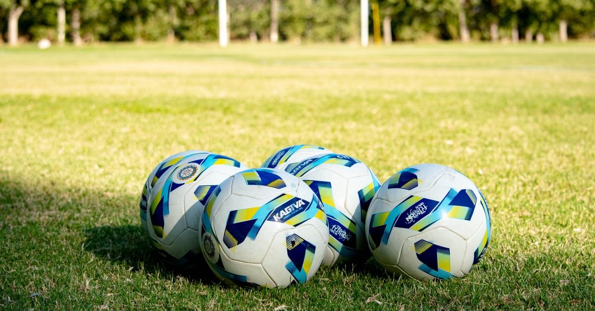 Bolas de futebol oficiais alinhadas sobre gramado de campo antes de uma partida