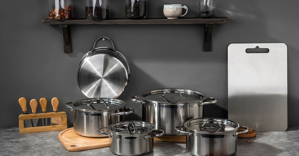 Jogo de panelas de aço inox sobre bancada de cozinha com tábua de madeira e cutelaria