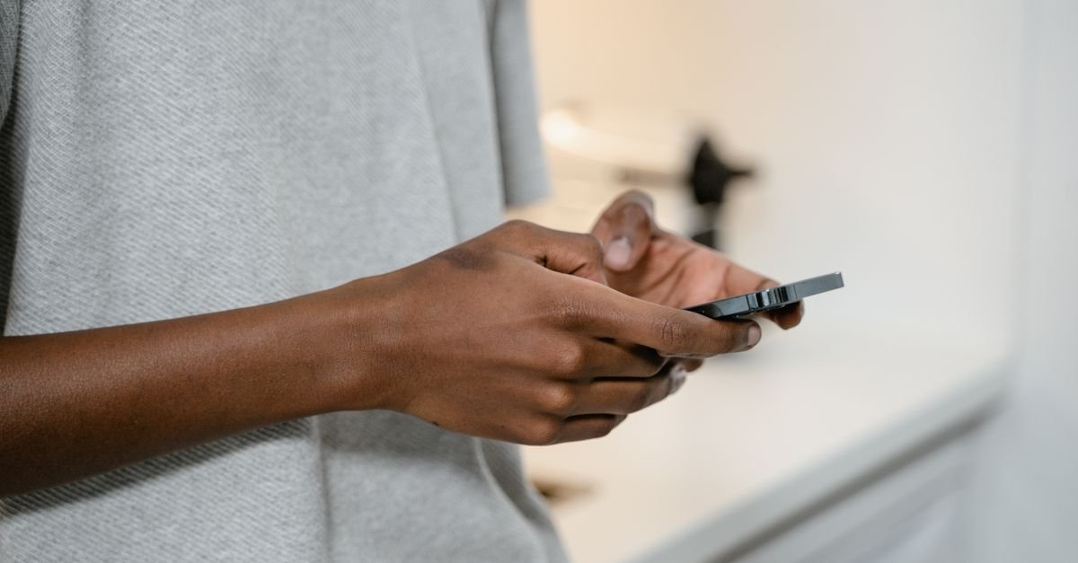 Mãos de uma pessoa usando um celular em ambiente interno
