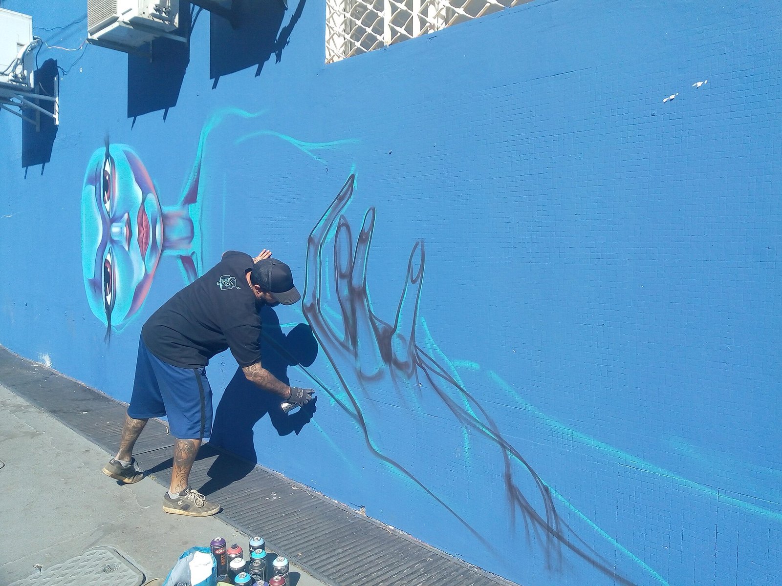 Artista pinta grafite com spray em muro azul durante intervenção urbana em Brasília