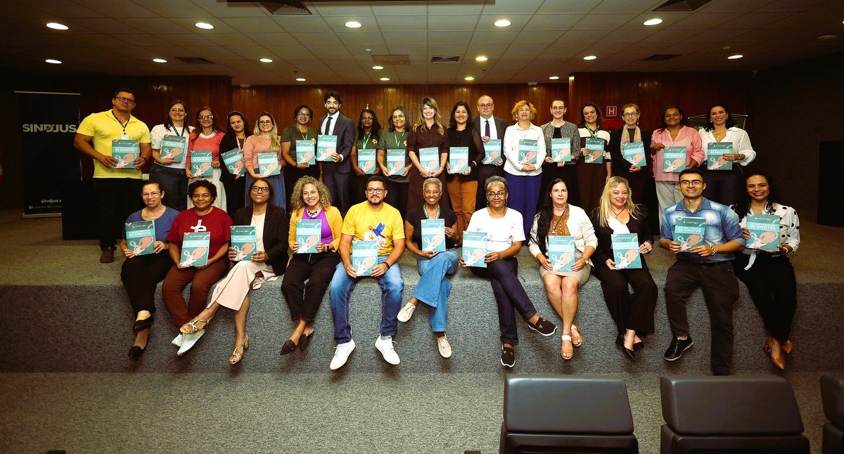 Participantes da capacitação posam com exemplares do guia Autismo e Proteção de Direitos no auditório do Fórum da Infância