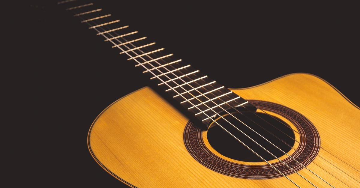 Violao acustico em close, com as cordas e a boca do instrumento iluminadas sobre fundo escuro