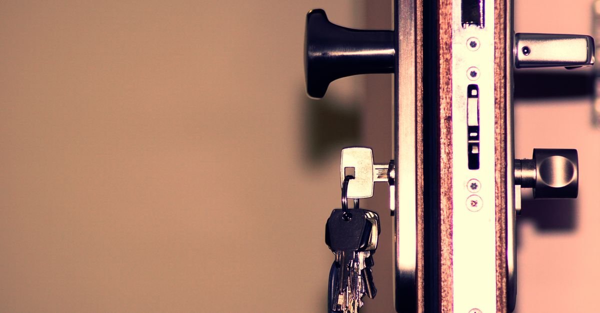 Chave inserida na fechadura de uma porta, com molho de chaves pendurado