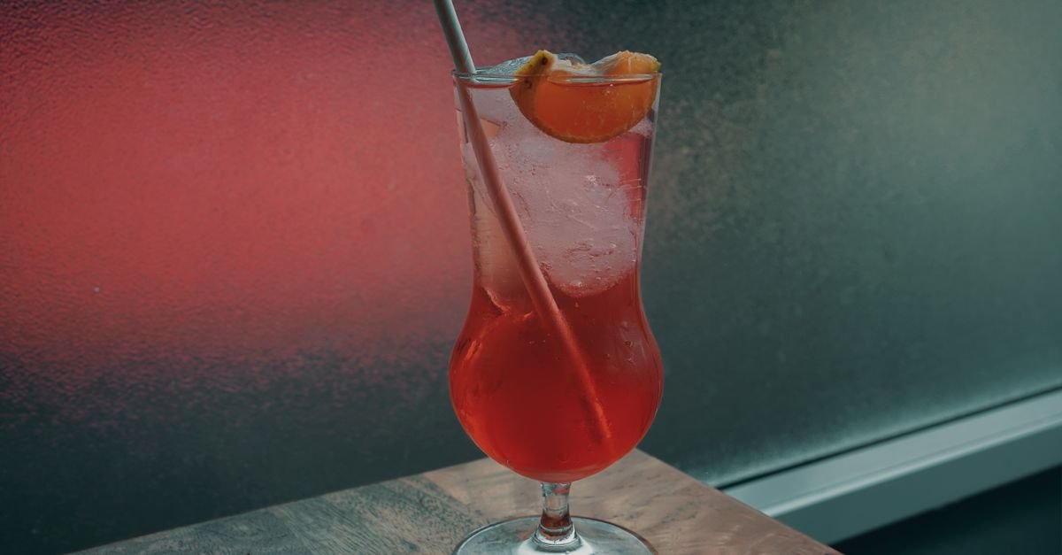 Coquetel sem álcool servido em taça alta, com fatia de fruta e canudo, sobre balcão de madeira