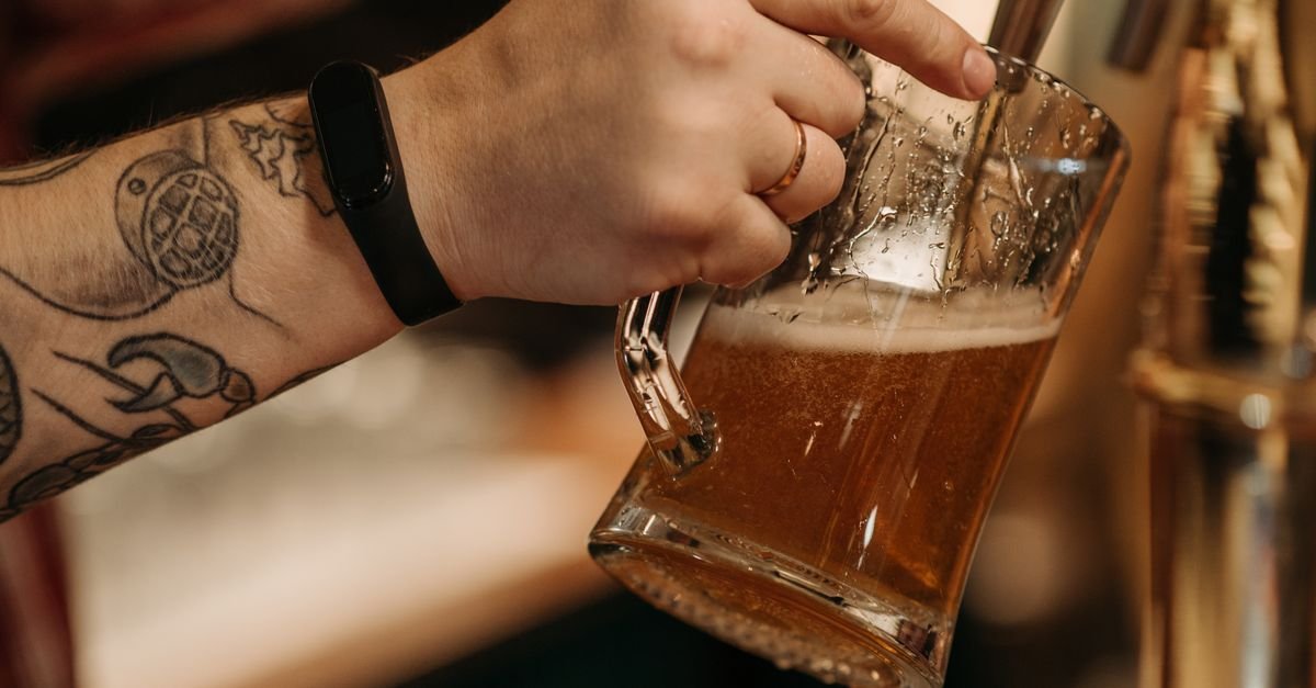 Mão tatuada servindo chope em caneca de vidro