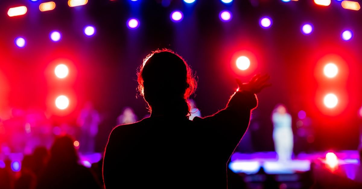 Silhueta de pessoa em show com luzes coloridas de palco ao fundo