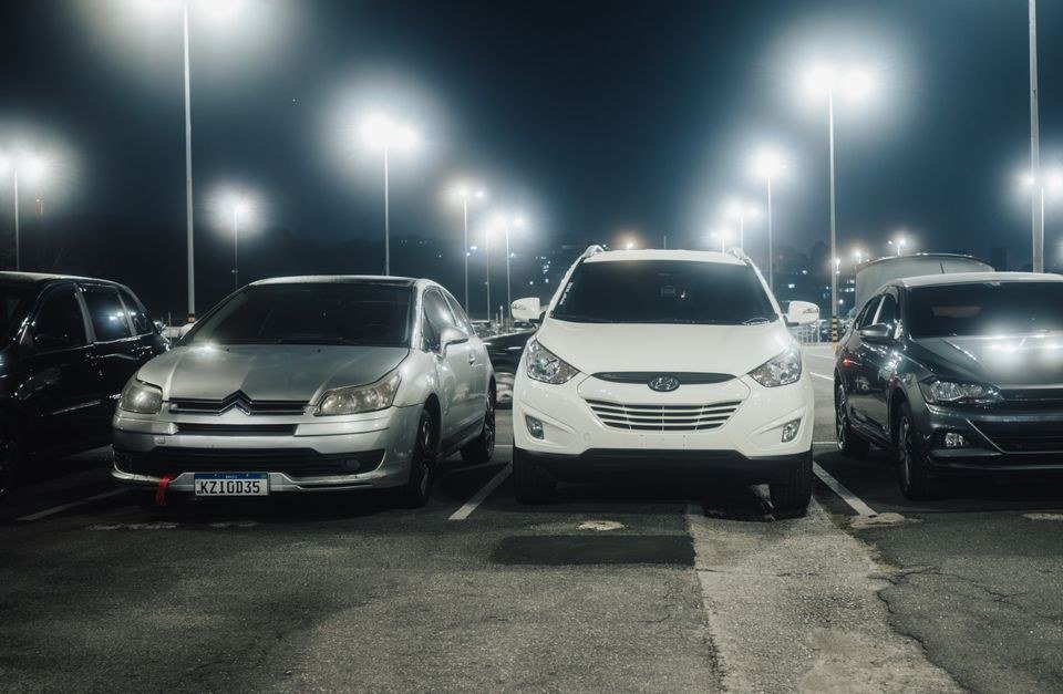 Carros estacionados à noite em estacionamento aberto iluminado por postes
