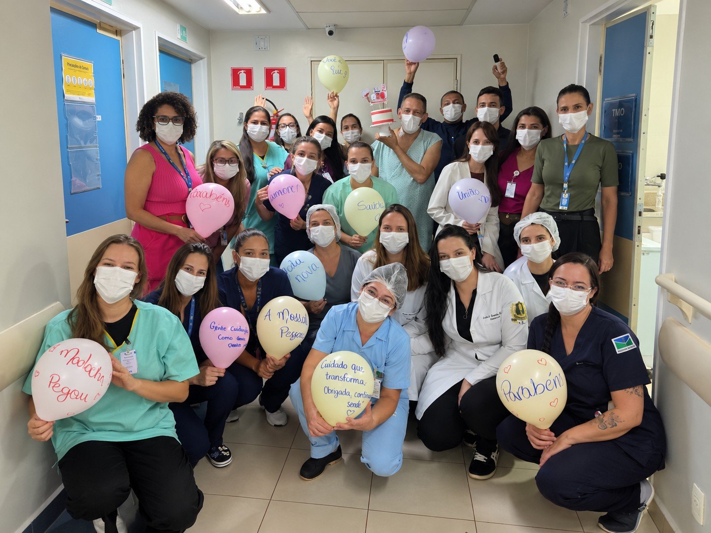 Equipe do Hospital de Base do DF e paciente em corredor do setor de transplante de medula, com balões escritos à mão