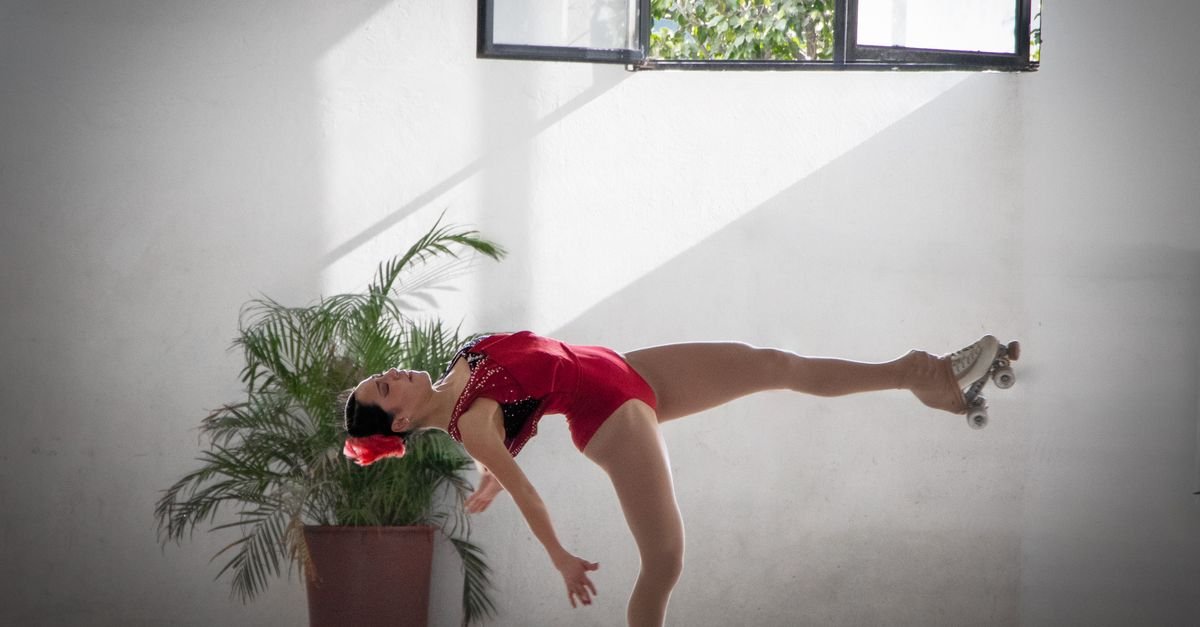 Patinadora de collant vermelho em pose de equilíbrio sobre patins de quatro rodas, em foto ilustrativa de patinação artística