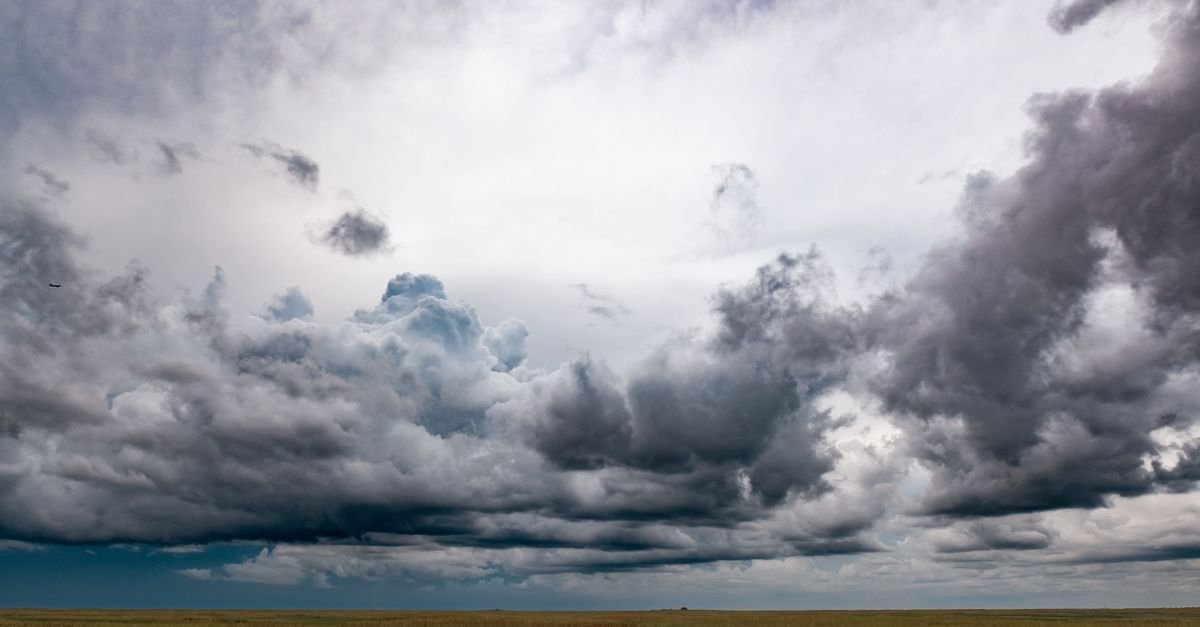 Nuvens carregadas de tempestade sobre campo aberto de vegetação rasteira e seca