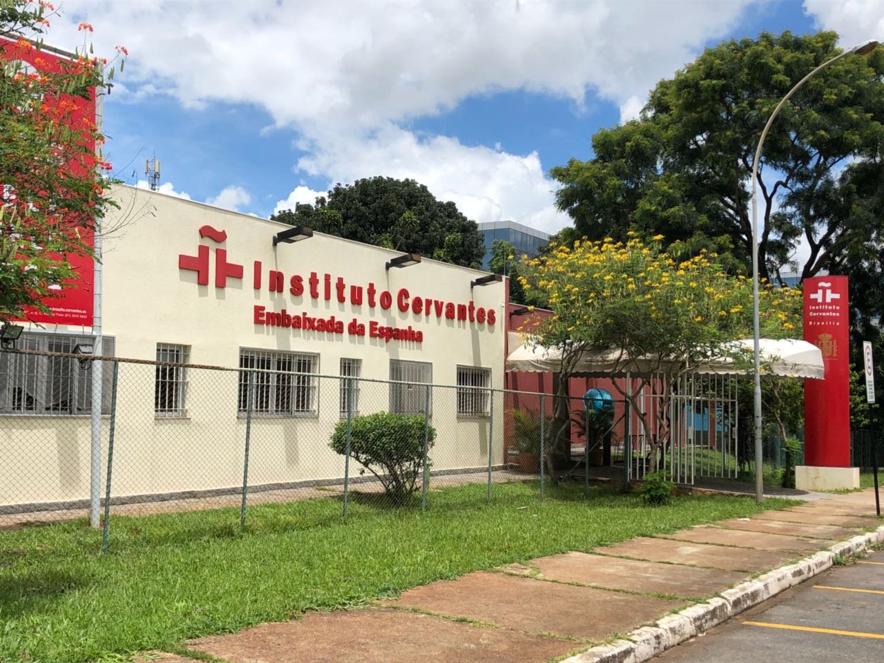 Fachada do Instituto Cervantes de Brasília, com letreiro vermelho, jardim e totem na entrada