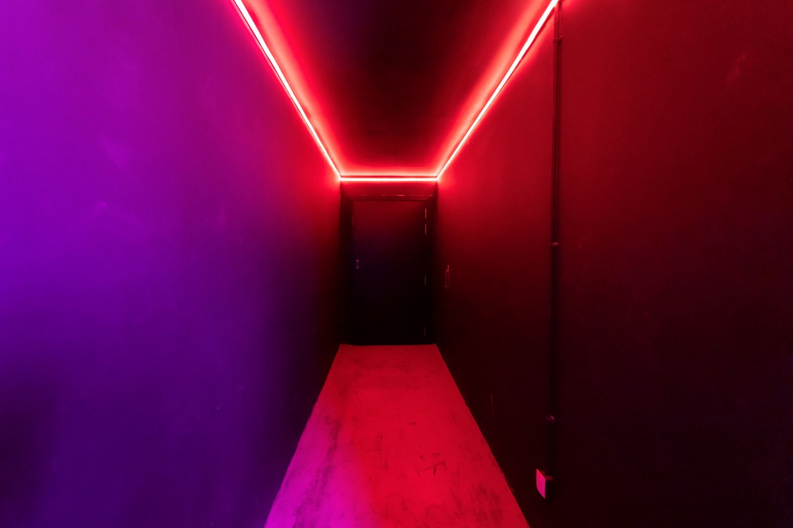 Corredor estreito iluminado por luz neon vermelha e roxa, imagem ilustrativa de ambiente escuro