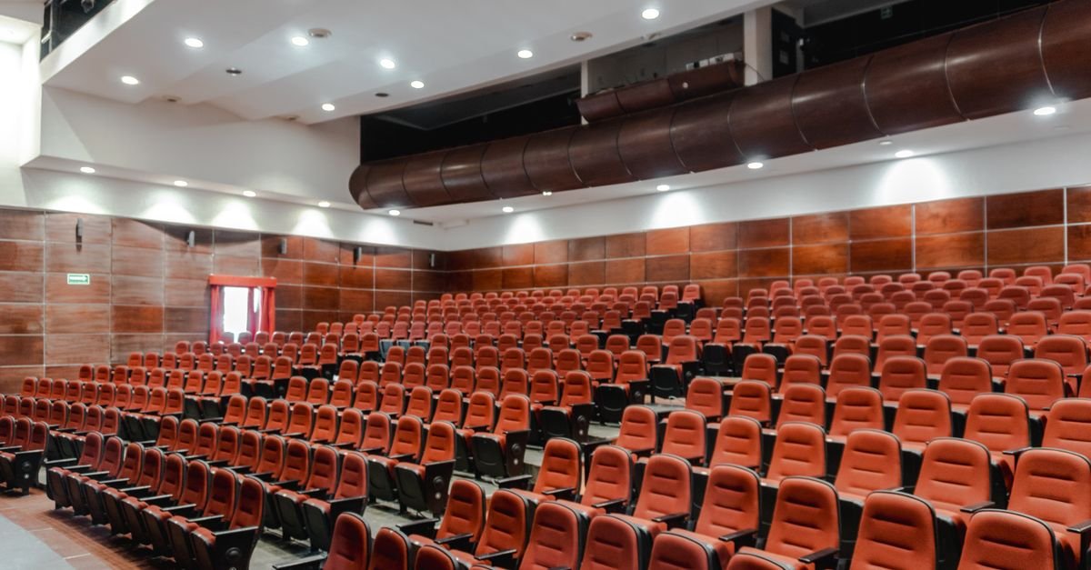 Auditório com fileiras de poltronas vermelhas vazias e paredes de madeira