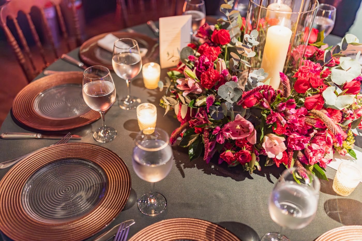 Mesa redonda de jantar com arranjo de flores vermelhas, velas e taças em salão de evento