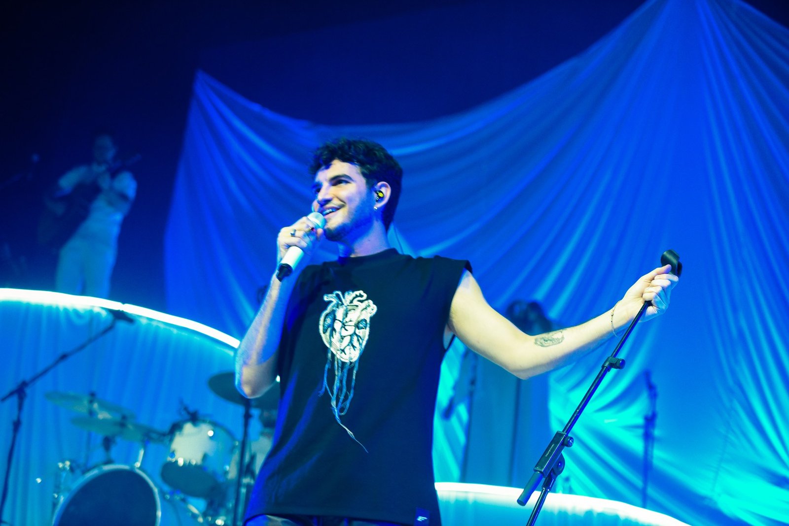 Jão cantando ao microfone em palco iluminado de azul, em show no Tom Brasil, em São Paulo