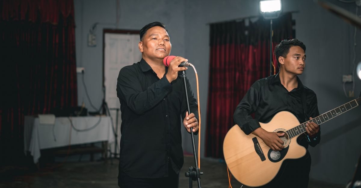 Vocalista ao microfone ao lado de músico tocando violão de aço em apresentação