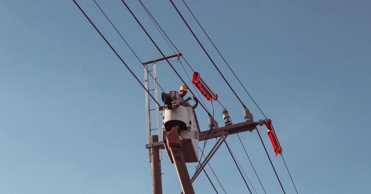 Eletricista em cesto aéreo faz manutenção em poste de rede elétrica