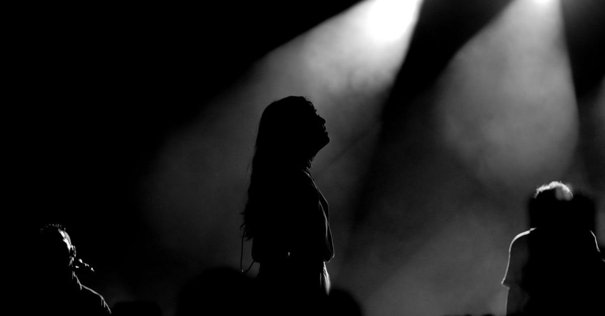 Silhueta de pessoas em show sob feixes de luz de palco em imagem preto e branco