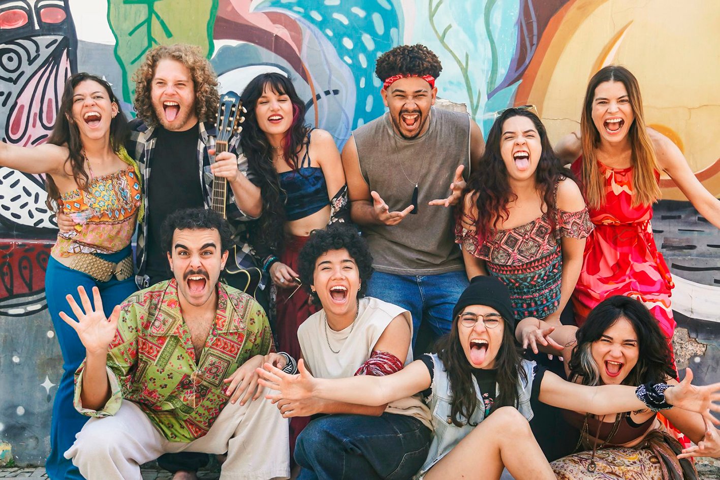 Elenco de dez jovens atores do musical Leo e Bia posa em frente a um muro grafitado, um deles com violao