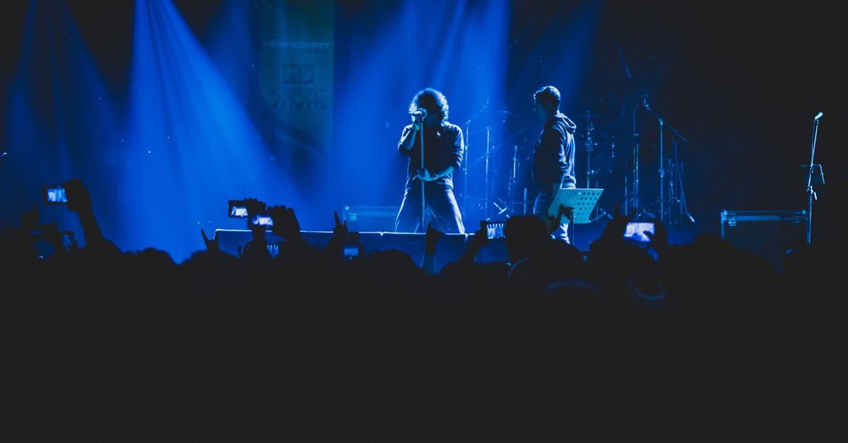 Vocalista e guitarrista no palco sob luz azul diante de plateia