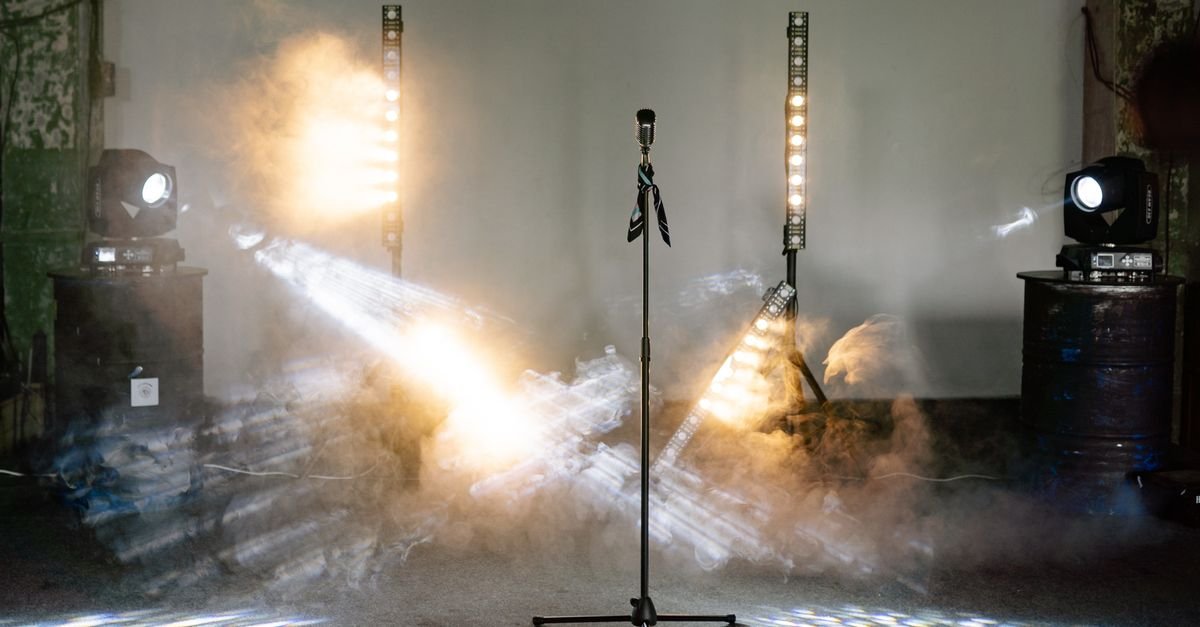 Microfone em pedestal no centro de palco iluminado por refletores e fumaça