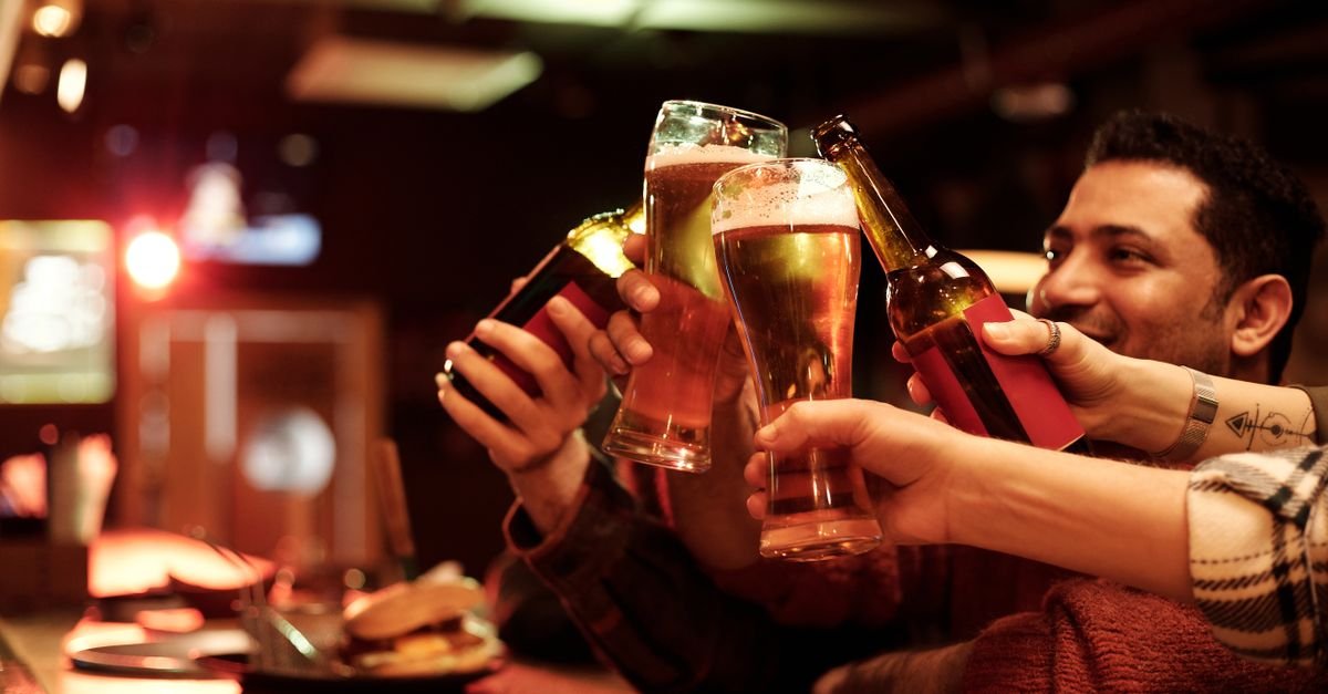 Grupo de amigos brindando com copos de cerveja em um bar com luz baixa