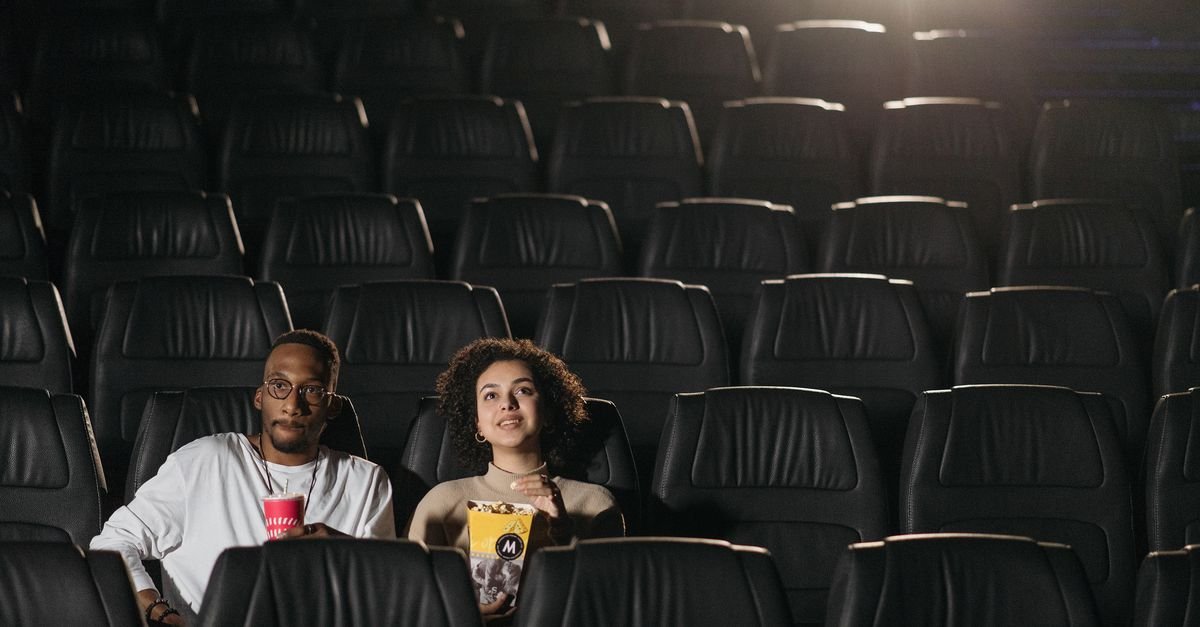 Sala de cinema com poltronas escuras e casal assistindo a um filme