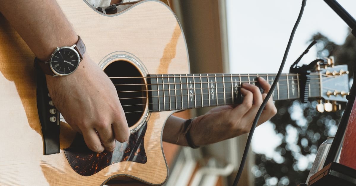 Mãos de músico tocando violão de aço em apresentação ao vivo