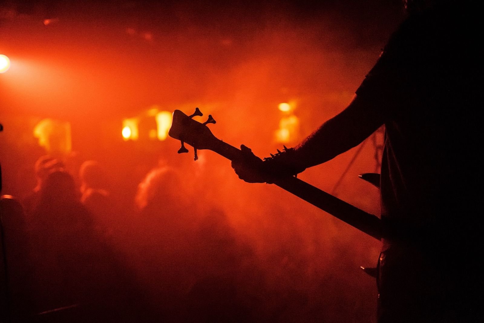 Silhueta de baixista diante de plateia em névoa vermelha, foto ilustrativa de show de metal