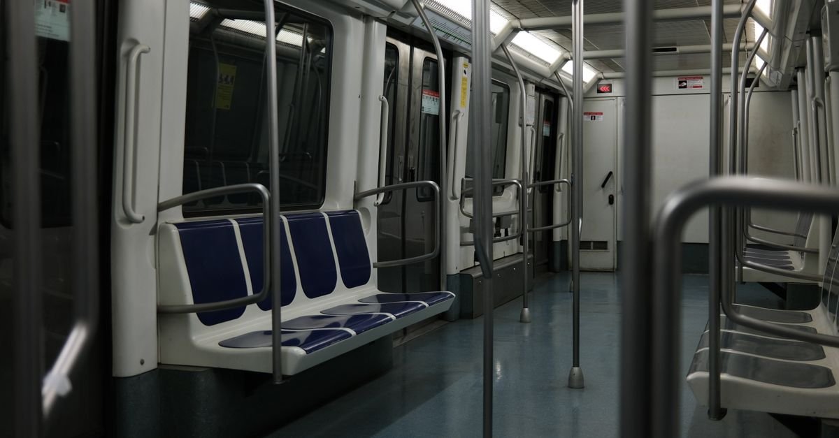 Interior de vagão de metrô vazio, com bancos azuis e barras de apoio metálicas