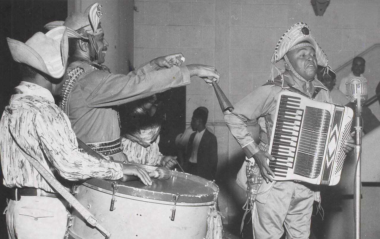 Luiz Gonzaga de chapéu de couro e sanfona ao microfone, ao lado de músicos com zabumba, em foto de arquivo em preto e branco