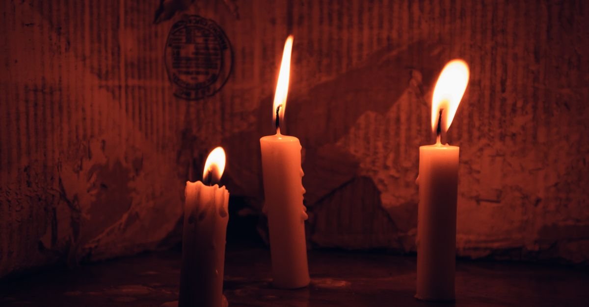 Três velas brancas acesas em ambiente escuro, com a chama iluminando a cera derretida