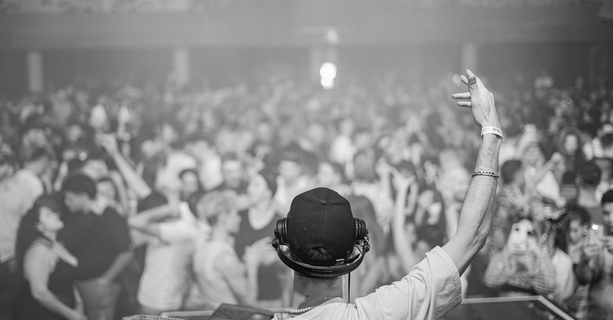 DJ de fones de ouvido e boné ergue o braço diante de pista lotada