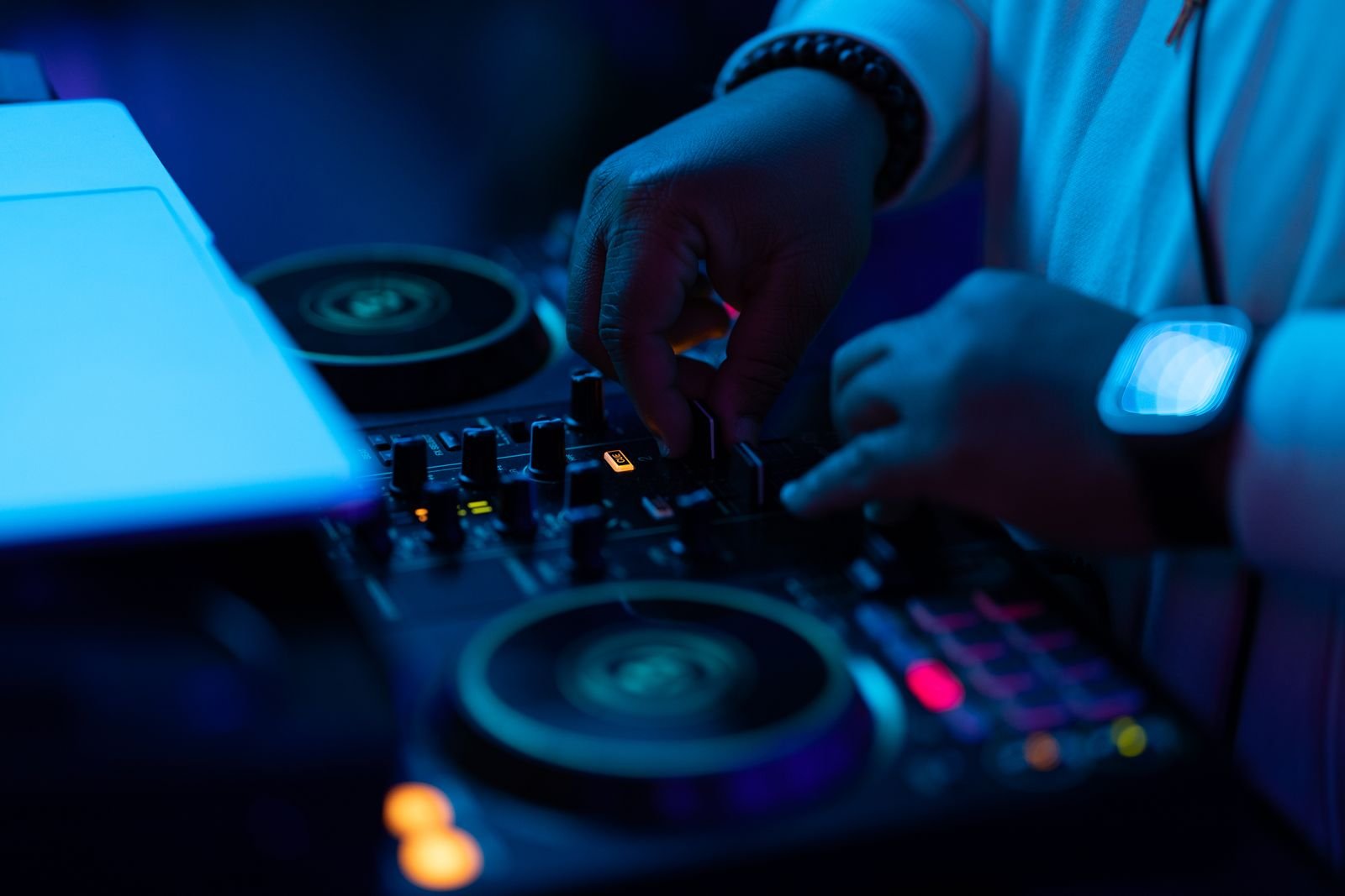 Mãos de um DJ ajustando os controles de um mixer sob luz azul