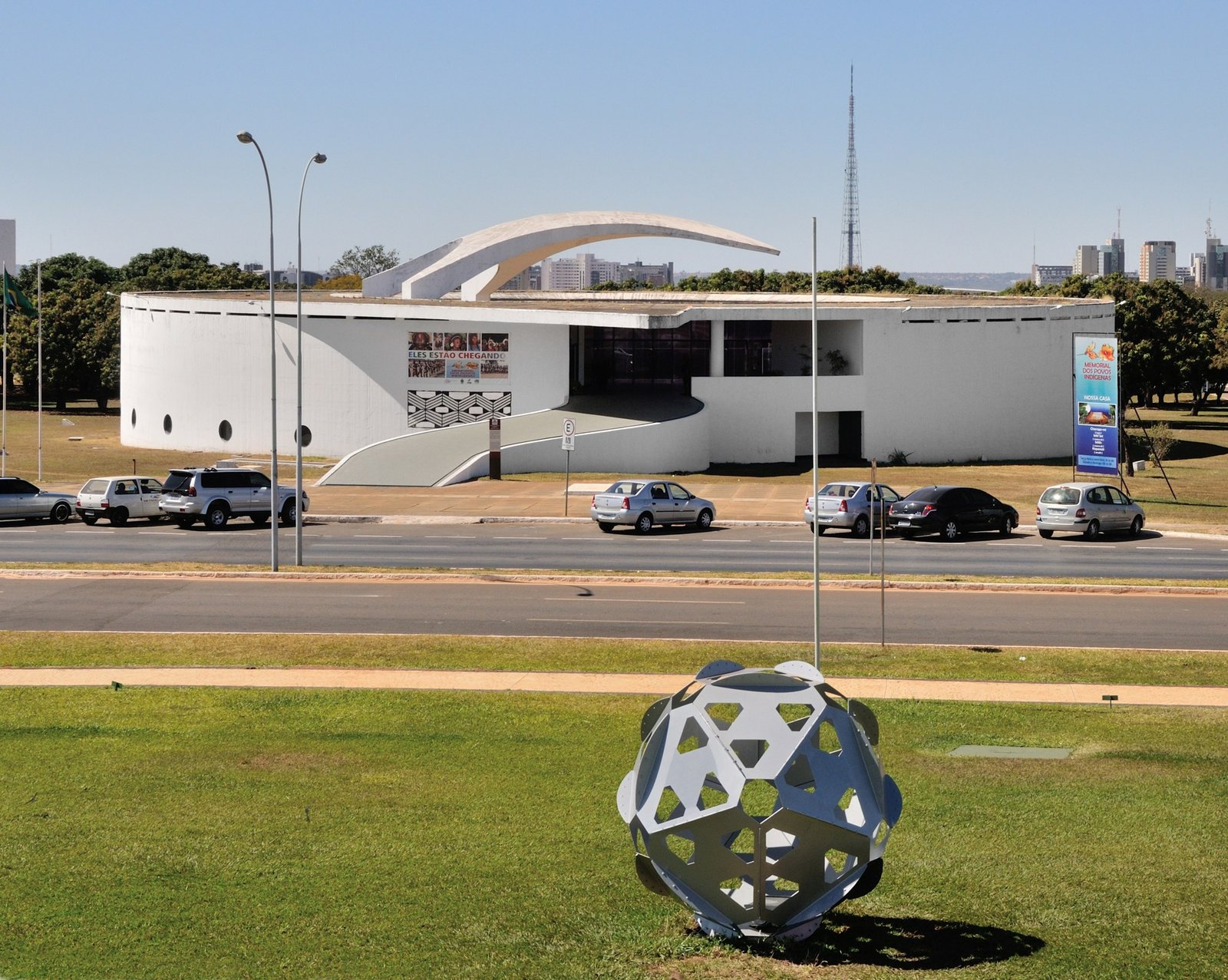 Fachada circular branca do Memorial dos Povos Indígenas, em Brasília, com a torre de TV ao fundo