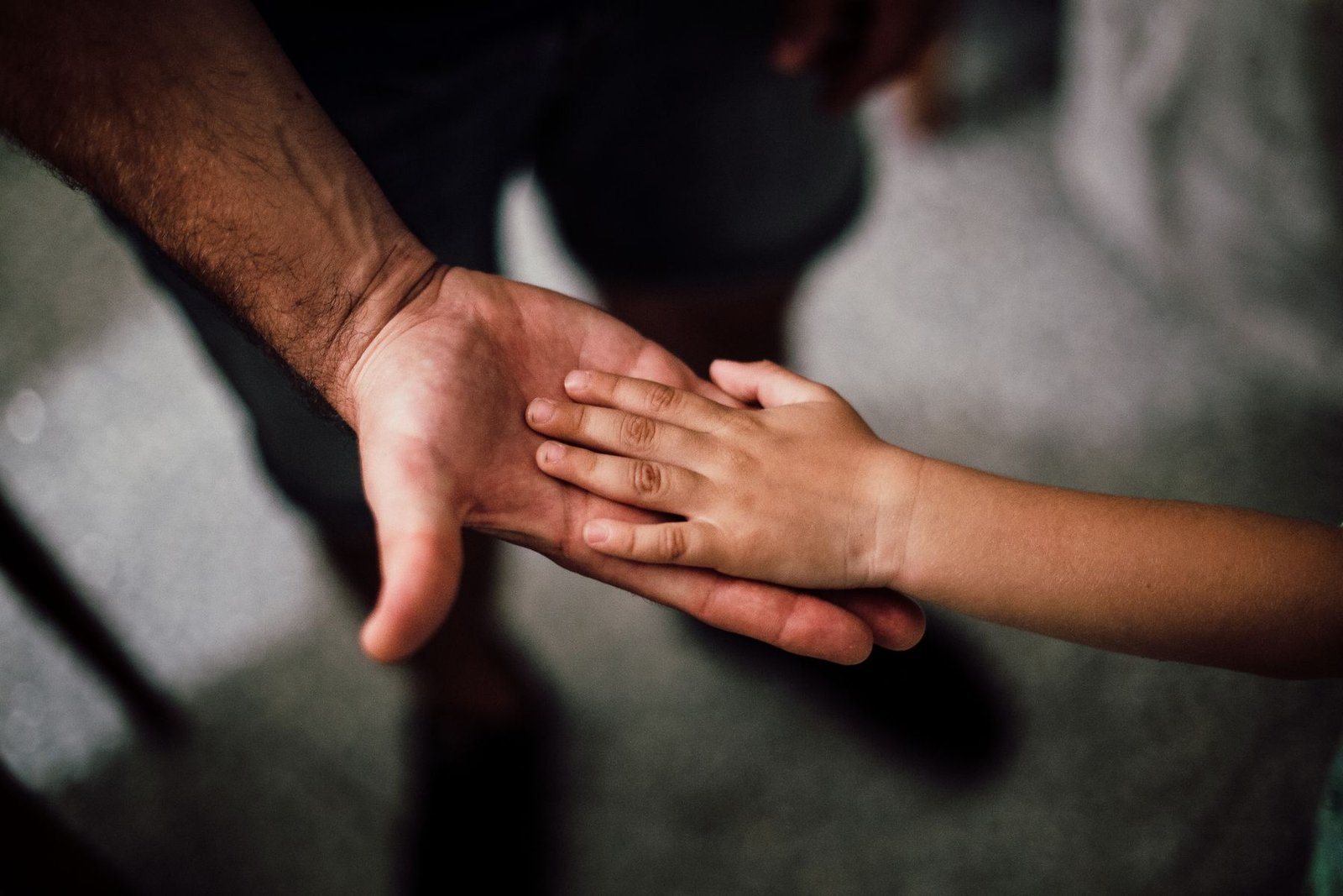 Mão de uma criança pousada sobre a mão aberta de um adulto, em close