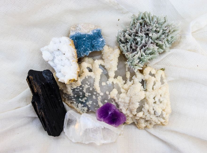Amostras de minerais e cristais de cores variadas dispostas sobre tecido branco
