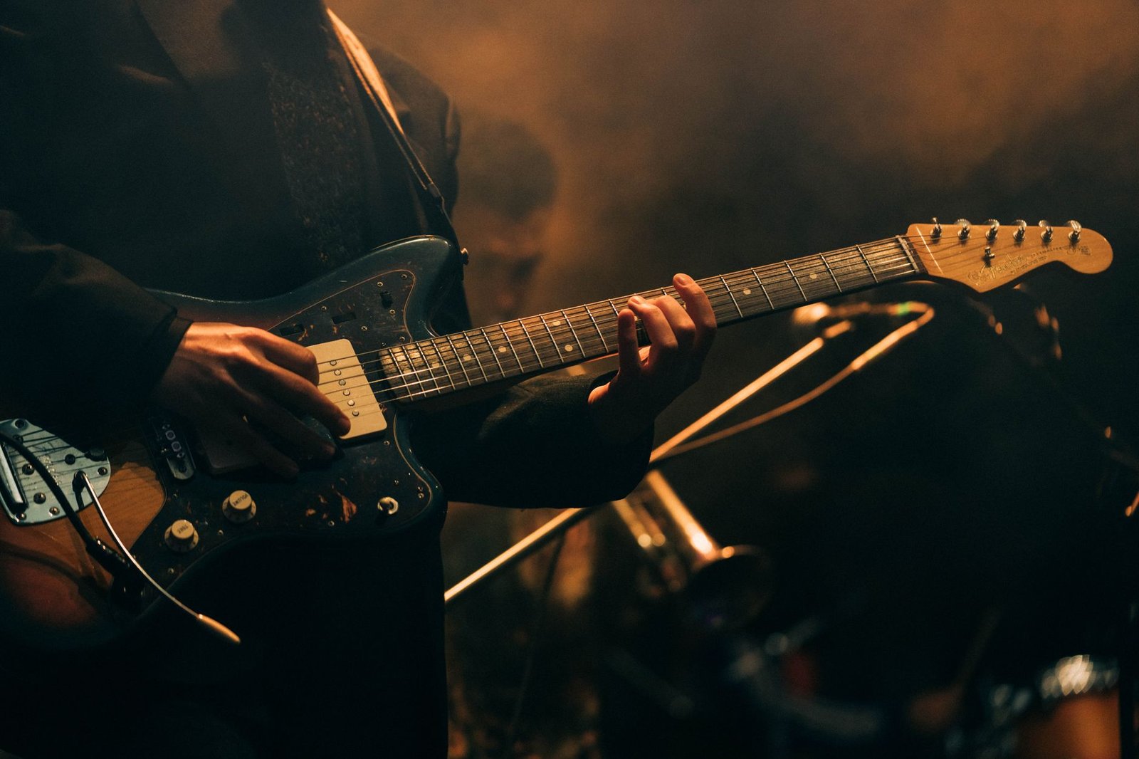 Guitarrista tocando uma guitarra elétrica em um palco com luz âmbar e fumaça ao fundo