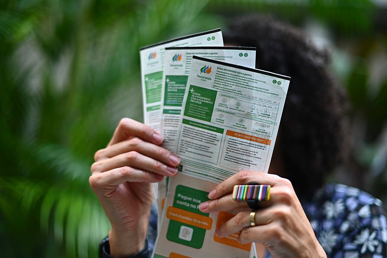 Mãos seguram folhetos informativos da Neoenergia Brasília com canais de atendimento ao consumidor