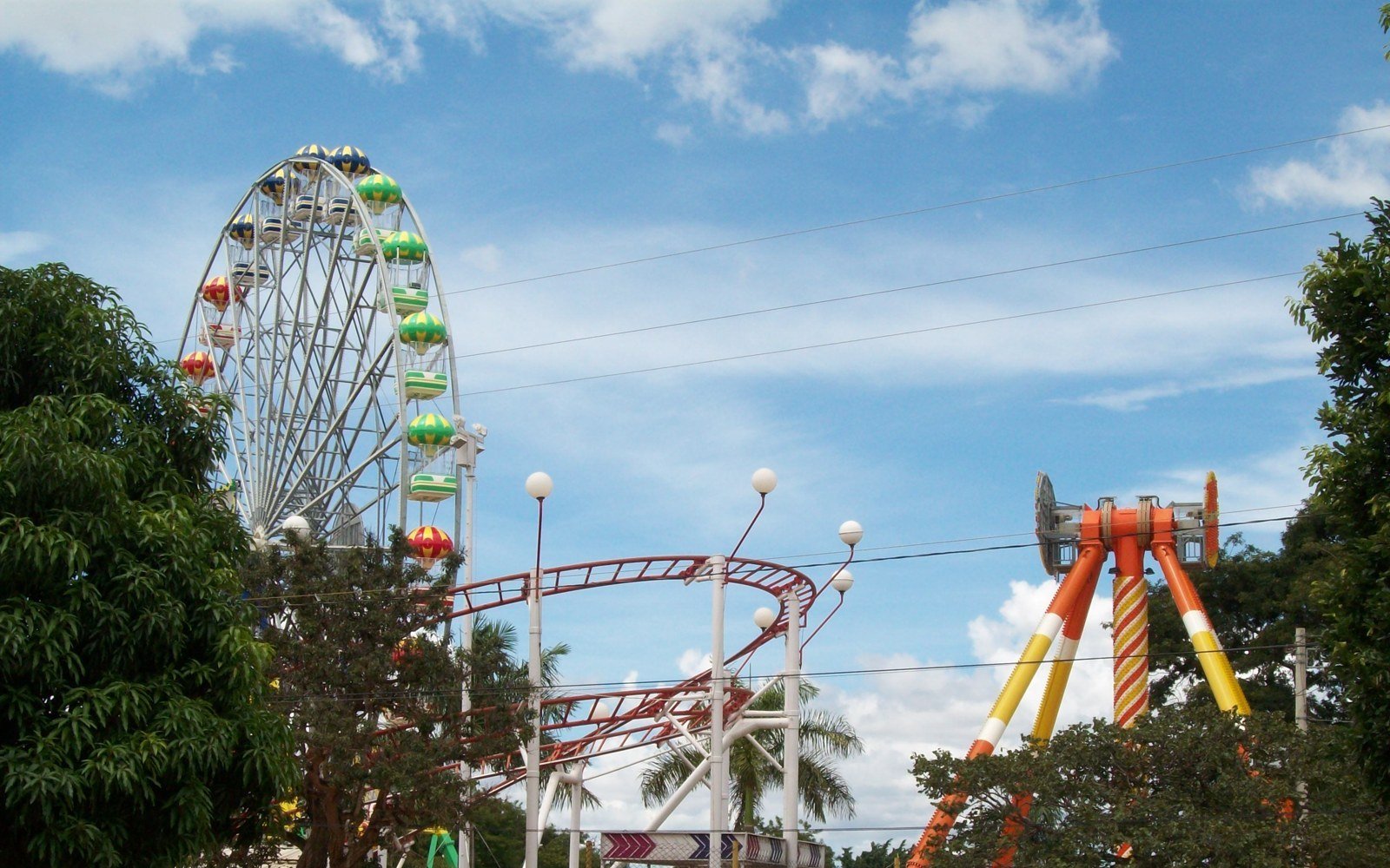 Roda-gigante, montanha-russa e brinquedo de pêndulo laranja do Nicolândia sob céu azul.