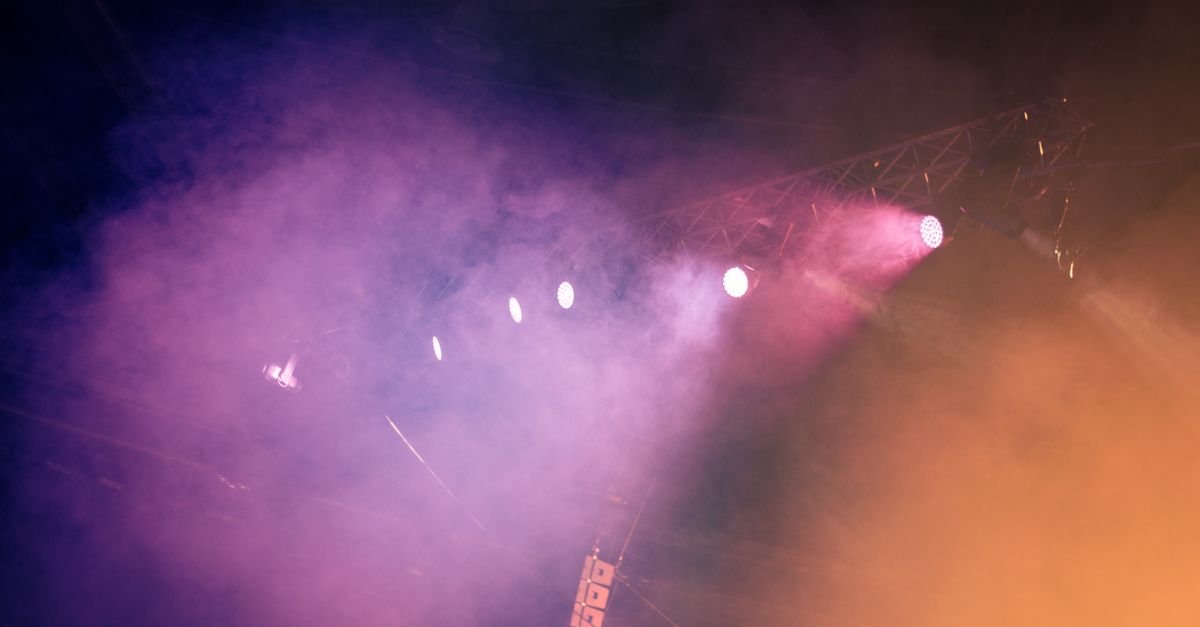 Luzes coloridas de palco iluminando a fumaca durante um show noturno