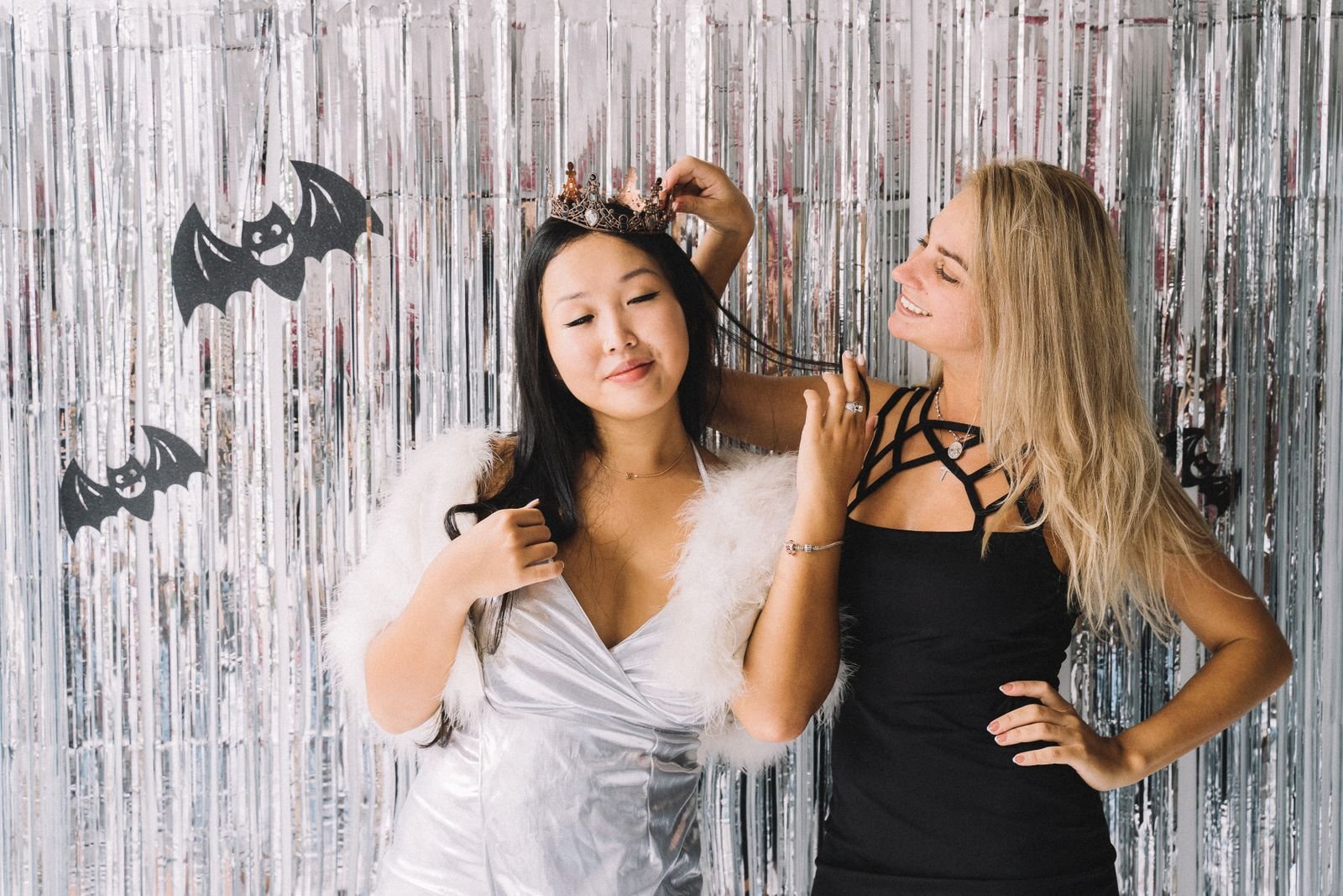 Duas mulheres fantasiadas diante de cortina prateada com morcegos de Halloween